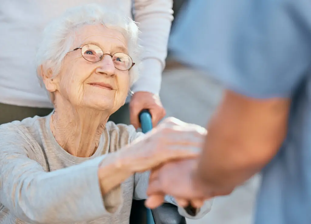 Holding hands, caregiver and senior woman in wheelchair for support outdoor in retirement home. Love, trust and healthcare nurse or medical wellness doctor for disability patient with kindness - The Williamsport Home