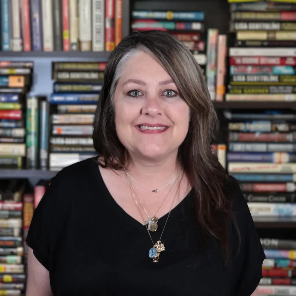 Smiling woman in a black top with shelves of colorful books behind her.